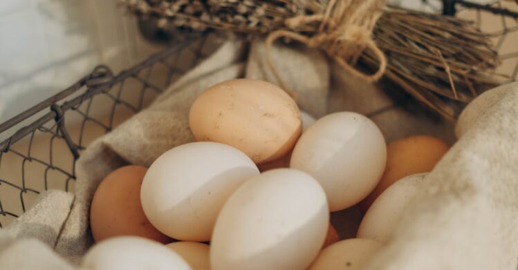 A collection of farm fresh eggs in a wire basket with dried herbs, exuding a rustic and organic feel.